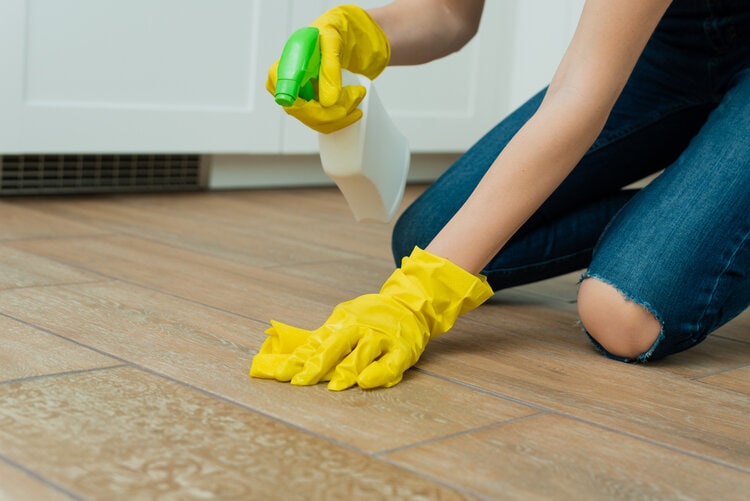 woman washing cleaning tile floor with spray and gloves
