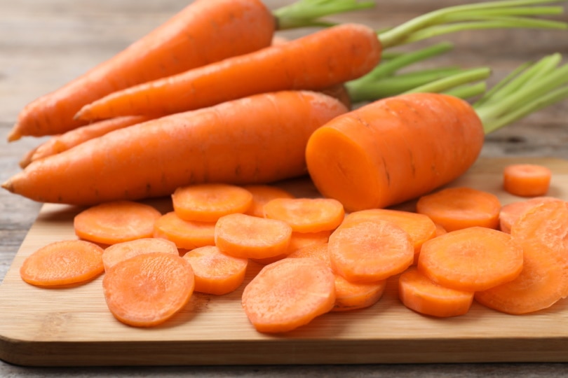 fresh and cut carrots on wooden board