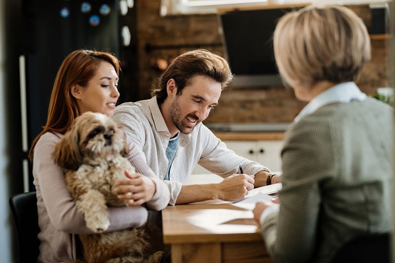happy man signing a pet isurance contract with his wife and dog on a meeting with financial advisor