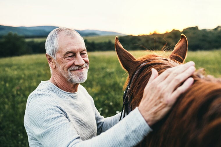a senior man stroking his horse outdoors