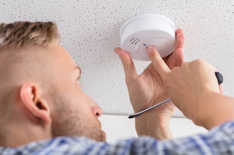 man installing smoke detector on ceiling wall at home