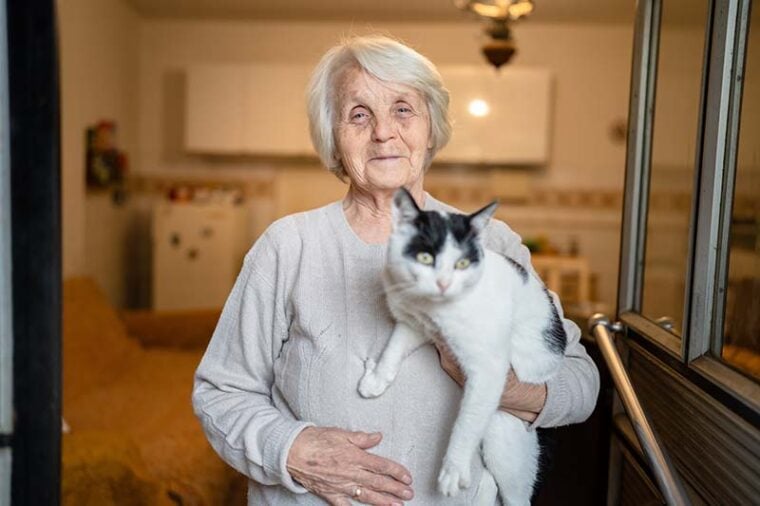 old woman standing at home holding a cat pet dementia alzheimer's disease