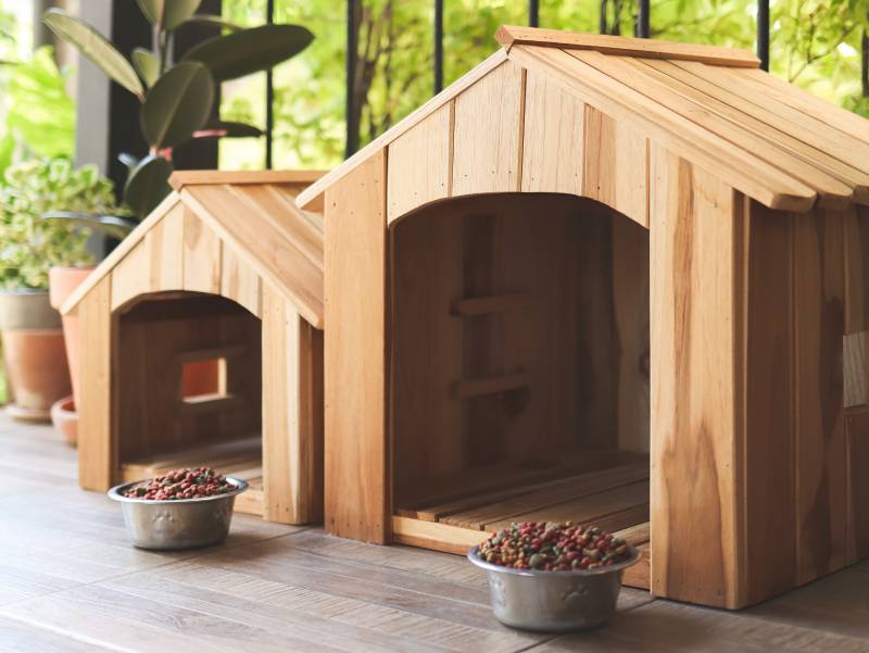 Side view of two empty wooden dog's houses with dog food bowls in balcony