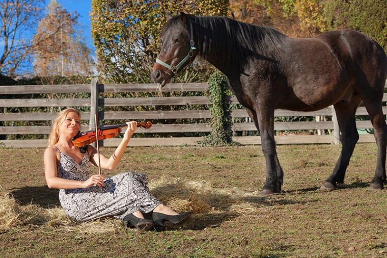 woman playing violin beside horse