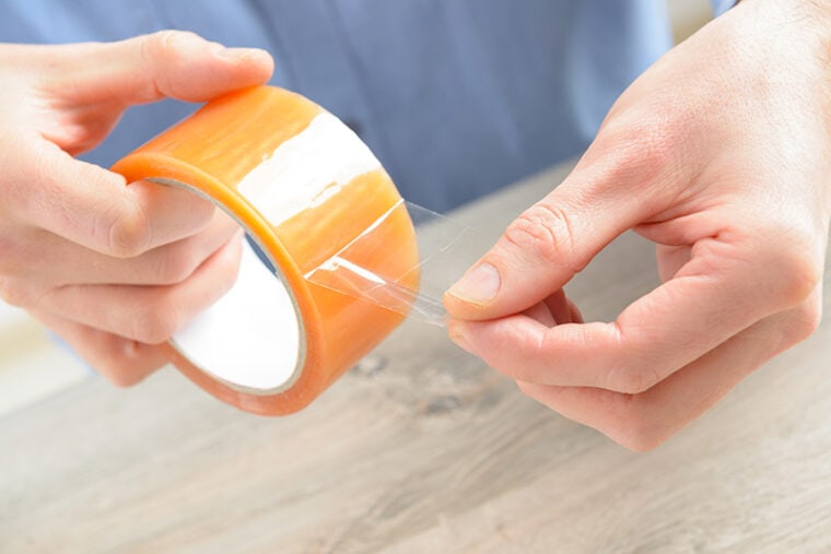 Hands with roll of transparent packaging, adhesive tape