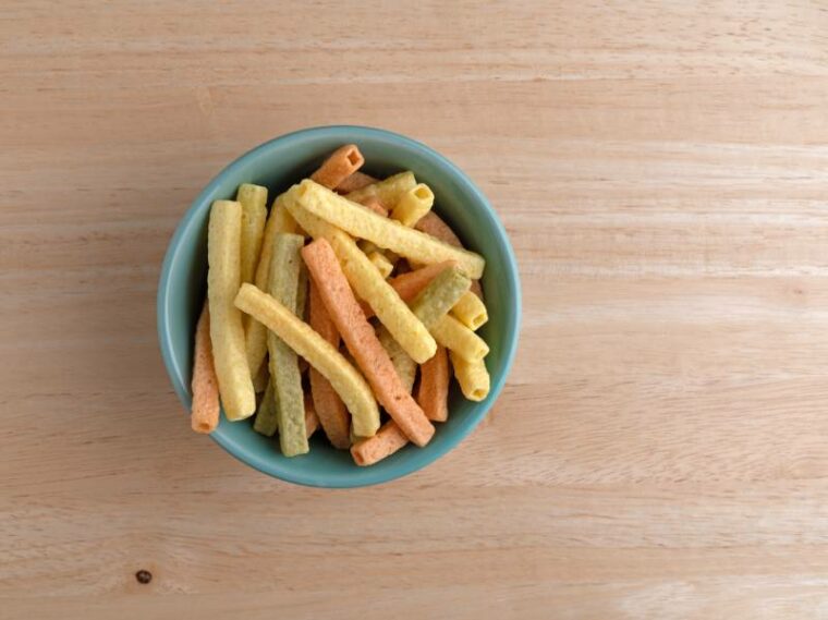 Top view of a green bowl filled veggie straws on a wood table