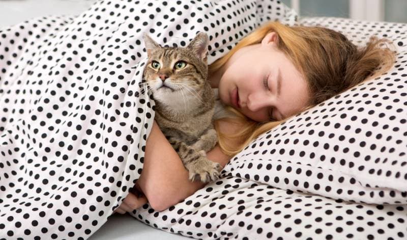girl hugging cat in bed