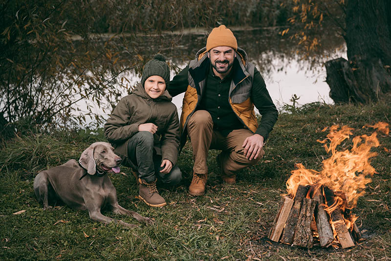 Father and son enjoying the bonfire with a weimaraner dog