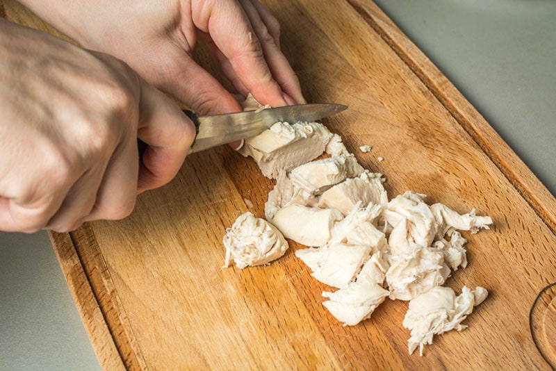 female hands cutting boiled chicken breast with knife