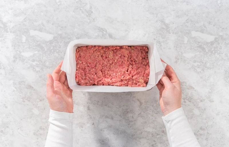 person preparing classic meatloaf in pan lined with parchment