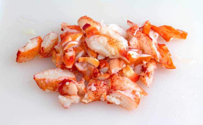 Chunks of cooked cut lobster meat on a plastic white cutting board